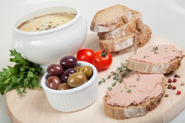 Homemade pate, olives, tomatoes and slices of bread on wooden board — Stock Photo, Image