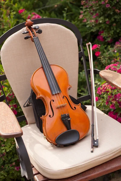 Violino e arco em uma cadeira no jardim — Fotografia de Stock