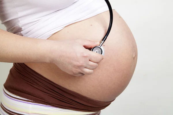 Pregnant woman listening her belly with stethoscope — Stock Photo, Image