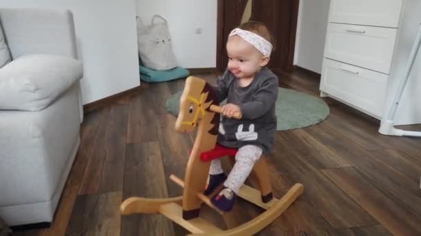 幸せな赤ちゃんの女の子は木製のロッキング馬で遊んでいる 子供の頃 家庭の概念でゲーム — ストック動画