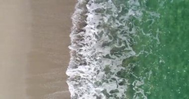 Köpüklü okyanus dalgalarının kumu yıkadığı tepeden aşağı manzara. Dalgalar kumsala vuruyor