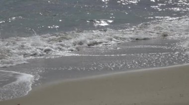 Kumsal, köpüklü okyanus, kumları yıkayan deniz dalgaları. Dalgalar kumsala vuruyor. Yavaş çekim 