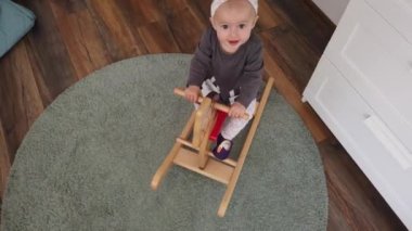 Tahta sallanan atın üstünde oynayan mutlu bir kız bebek. Çocukluk, evde oyun konsepti