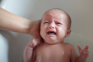 Yeni doğan bebeği annesi tarafından banyo ettiriliyor. Yeni doğmuş bebek banyoda ağlıyor.
