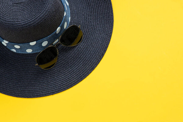 Blue hat with ribbon and sunglasses on yellow background. Summer concept. Top view with copy space