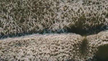 Tropikal plajın yukarıdan görünen manzarası köpüklü okyanus dalgaları kum yıkıyor. Dalgalar kumsala vuruyor