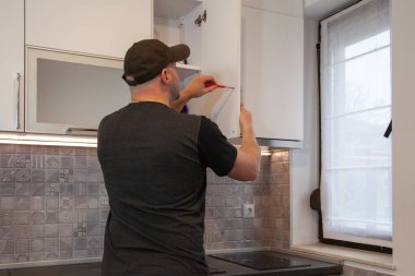 Marangoz yeni mutfakta çalışıyor. Tamirci mutfakta kapı tamir ediyor.