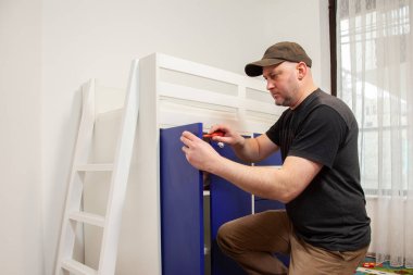 Carpenter working on new children bed. Handyman fixing a door in a wardrobe