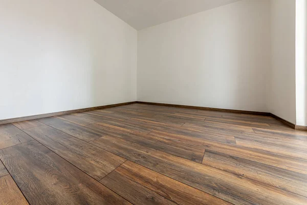 Laminated wood floor with white wall. Empty room with floating laminate in new apartmen