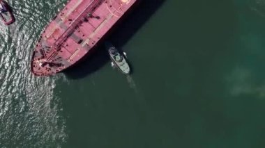 Top down view of Tug boats assisting big cargo ship. Large cargo ship enters the port escorted by tugboats.