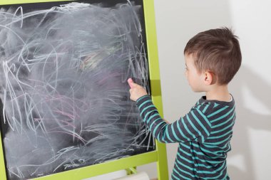 Little boy drawing with a chalk on chalk board with left hand