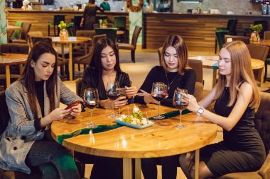 Bir grup bayan arkadaş restoranda bir masada oturmuş akıllı telefonlar kullanıyorlar..
