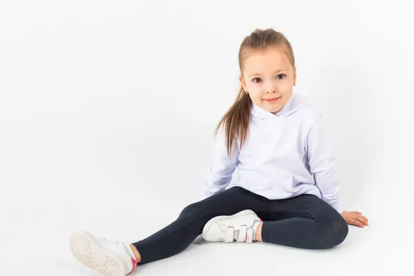 白い空のパーカーを着た女の子が白い背景に座っています 子供たちはうっとうしい — ストック写真