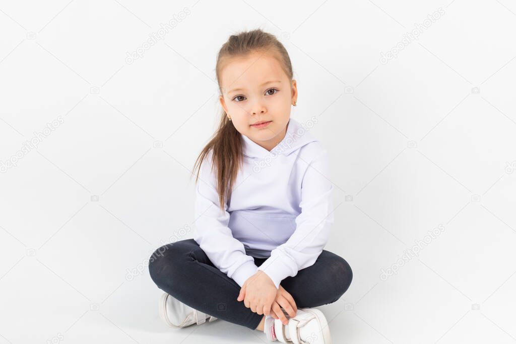 Girl in a white blank hoodie sits on a white background. Kids hoodies mockup.