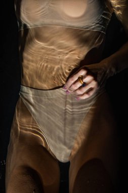 Bej iç çamaşırlı seksi kadın karanlık bir arka planda suya uzanıyor..