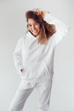 Beyaz kapüşonlu ve eşofmanlı kalın kıvırcık saçlı, gülümseyen kadın. Model.