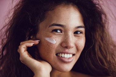 Kıvırcık saçlı ve yüzünde krem olan bir kadının portresi..