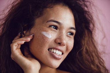 Kıvırcık saçlı ve yüzünde krem olan bir kadının portresi..