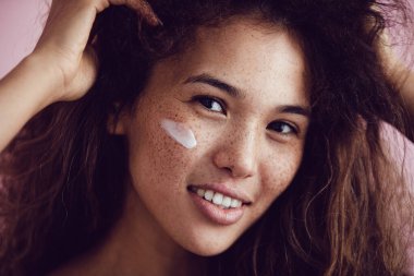Kıvırcık saçlı ve yüzünde krem olan bir kadının portresi..