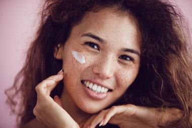 Kıvırcık saçlı ve yüzünde krem olan bir kadının portresi..