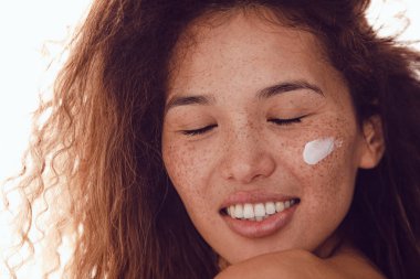 Gülümseyen kadın portresi kıvırcık saçlı ve yanağında nemlendirici olan çilli..