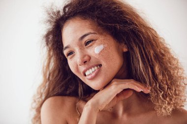 Nemlendirici yüz kremi kullanan gür kıvırcık saçlı ve çilli bir kadının portresi..