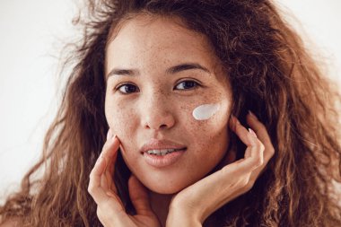 Yüzünde krem olan genç ve güzel bir kadın.