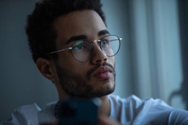 Gözlüklü, akıllı telefon kullanan Afro-Amerikan bir adamın portresi..