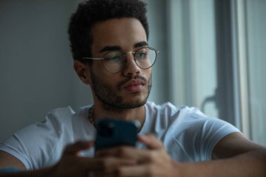 Gözlüklü, akıllı telefon kullanan Afro-Amerikan bir adamın portresi..