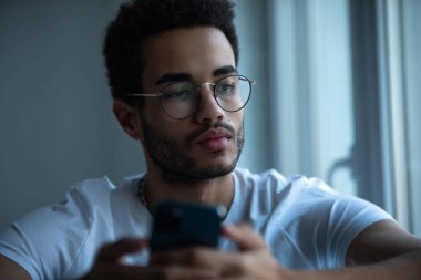 Gözlüklü, akıllı telefon kullanan Afro-Amerikan bir adamın portresi..