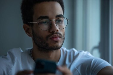 Gözlüklü, akıllı telefon kullanan Afro-Amerikan bir adamın portresi..