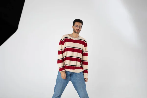 Young african american man in eyeglasses and a striped sweater stands on a white background. — Stock Photo, Image