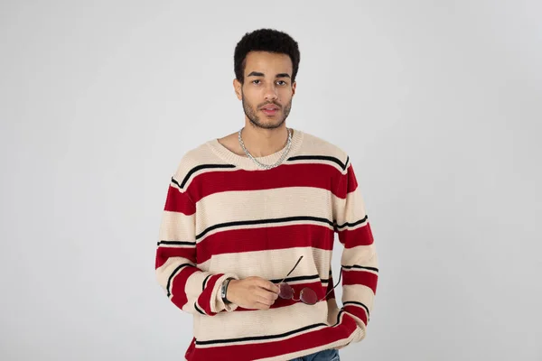 Young african american man in eyeglasses and a striped sweater stands on a white background. — Stock Photo, Image