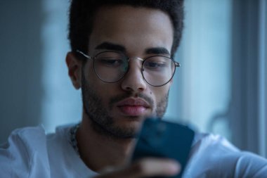 Gözlüklü, akıllı telefon kullanan Afro-Amerikan bir adamın portresi..