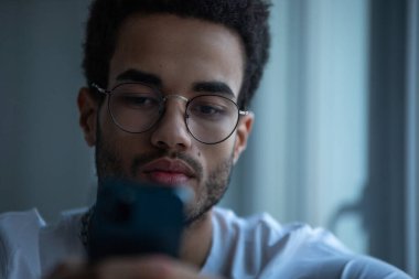 Gözlüklü, akıllı telefon kullanan Afro-Amerikan bir adamın portresi..