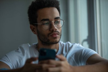 Gözlüklü, akıllı telefon kullanan Afro-Amerikan bir adamın portresi..