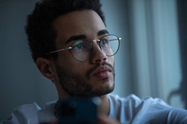 Gözlüklü, akıllı telefon kullanan Afro-Amerikan bir adamın portresi..