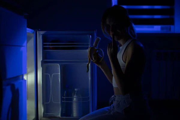 Mujer Come Una Banana Mientras Está Sentada Cerca Refrigerador Abierto — Foto de Stock