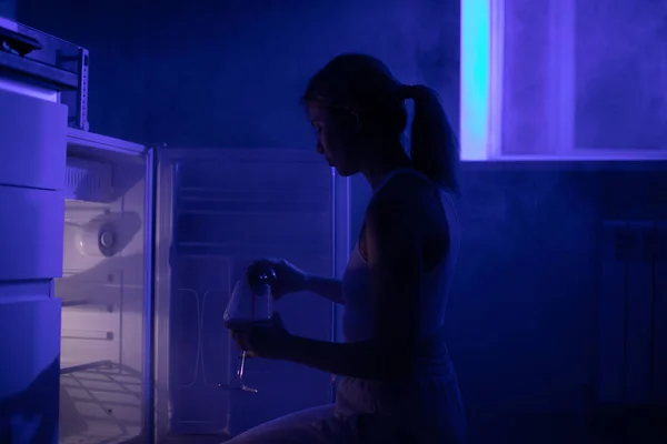 暗闇の中でオープン冷蔵庫の前に座ってワインを飲む悲しい女性 — ストック写真