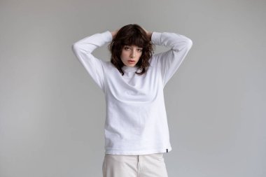 Beyaz uzun kollu tişörtlü kıvırcık saçlı genç kadın beyaz arka planda duruyor. Model.