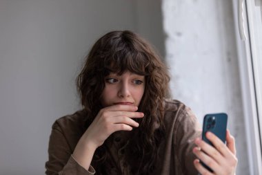 Kıvırcık genç kadın akıllı telefon kullanarak görüntülü konuşma yapıyor..