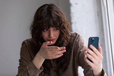 Kıvırcık genç kadın akıllı telefon kullanarak görüntülü konuşma yapıyor..