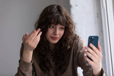 Kıvırcık genç kadın akıllı telefon kullanarak görüntülü konuşma yapıyor..