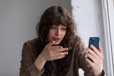 Kıvırcık genç kadın akıllı telefon kullanarak görüntülü konuşma yapıyor..