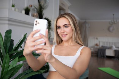 Spor kıyafetli çekici sarışın kadın evde selfie çekiyor..