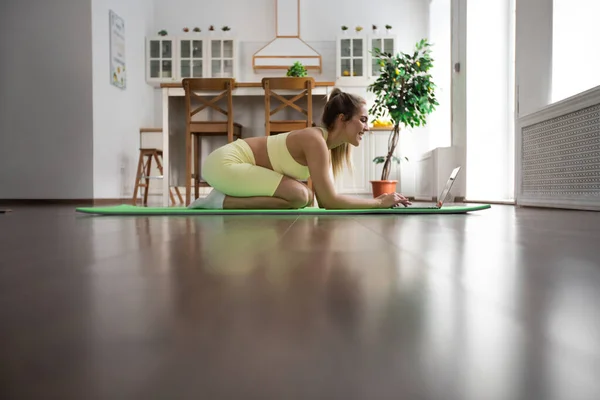 Sportliche Frau Sitzt Auf Yogamatte Und Schaut Auf Laptop — Stockfoto