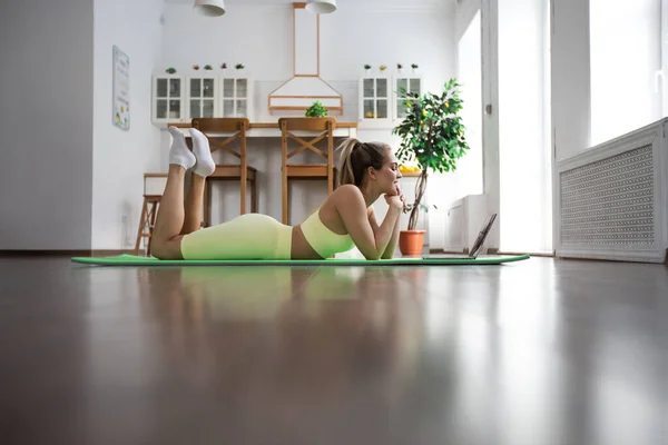 女运动员躺在瑜伽垫上 看着笔记本电脑 — 图库照片