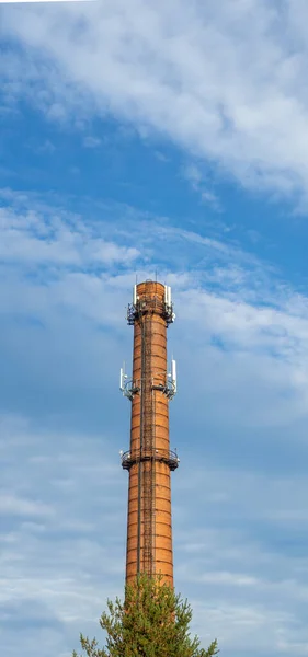 An old red brick factory chimney with various modern antennas for the Internet and mobile communications against cloudy sky.