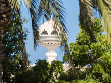 Palmiye yapraklarının arasından Riyam Park anıtına bakın. Muscat, Umman..
