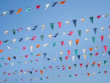 Renkli çok renkli üçgen bayraklar gün boyunca mavi gökyüzüne karşı iplerde sallanıyor. Festival bayrakları.